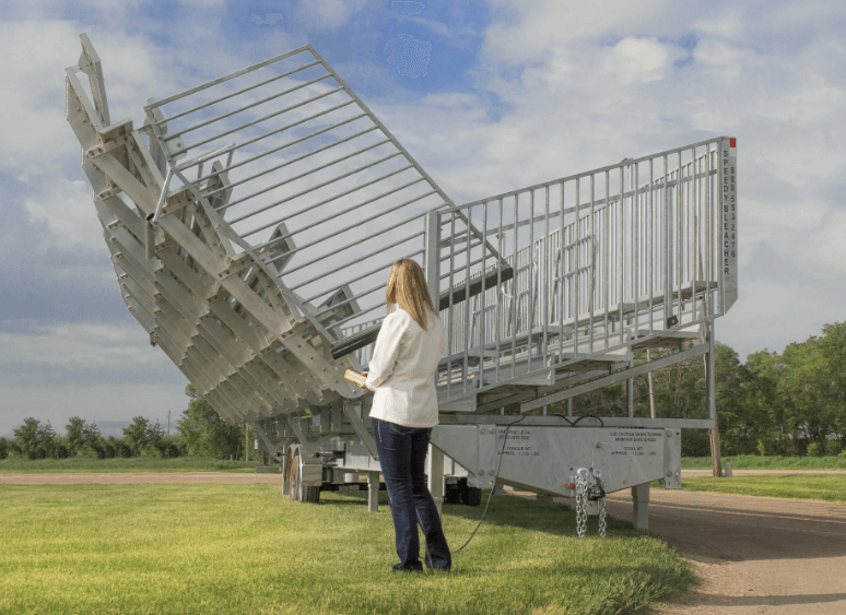 Single operator using hydraulic controls to raise portable aluminum bleachers from trailer for fast event setup.